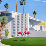 Vibrant artwork depicts an architecturally designed mid-century modern home adorned with pink flamingo garden ornaments, palm trees, and cactus gardens