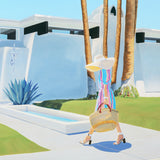 Woman in a colorful dress and hat walking by a pool with palm trees in the background
