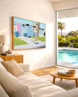 Modern living room with a painting on the wall and a view of a pool and palm trees outside.
