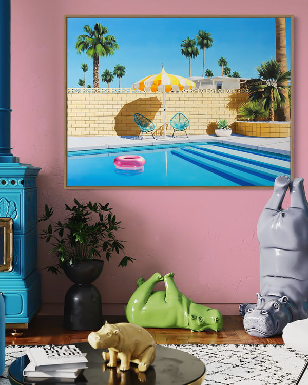 A chic room with an eye-catching pool scene artwork on the wall featuring a yellow and white striped umbrella and a pink inflatable pool ring floating on a crystal-clear swimming pool in Palm Springs